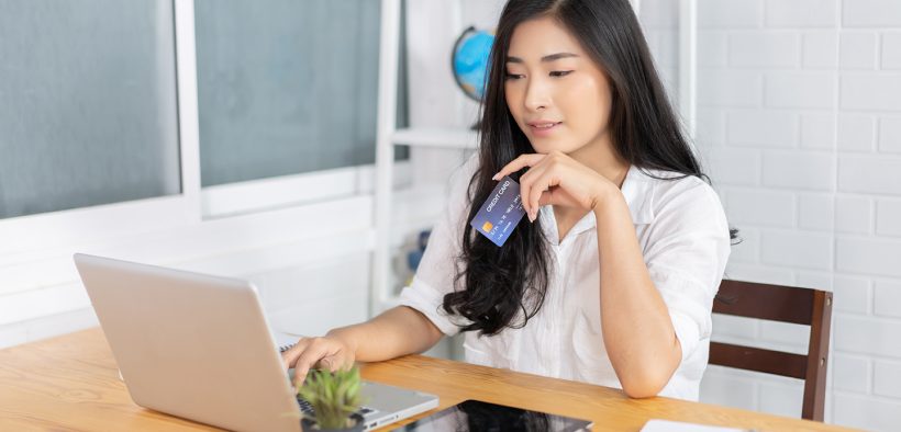 Image of a young woman sitting at her computer online shopping holding a credit card in her hand for E-commerce in Asia Growth of the Online Marketplace blog post