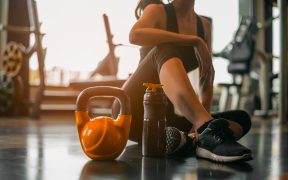 Woman sitting on a gym floor with fitness equipment around her.